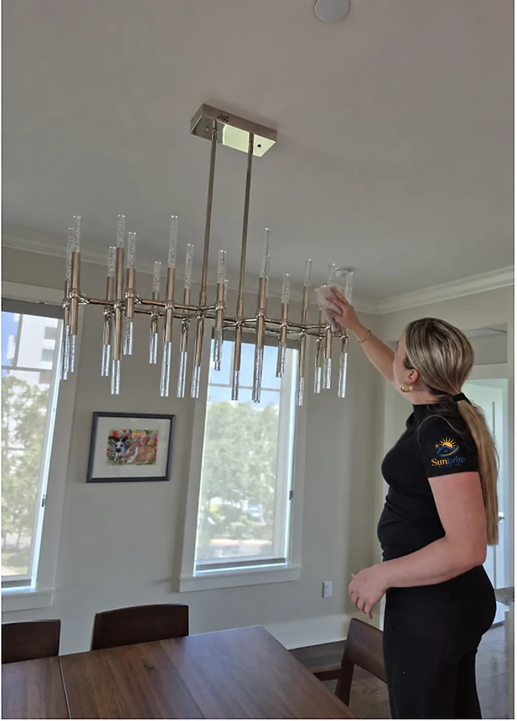 Sunbrite Cleaning LLC team member wiping a crystal chandelier above a dining table