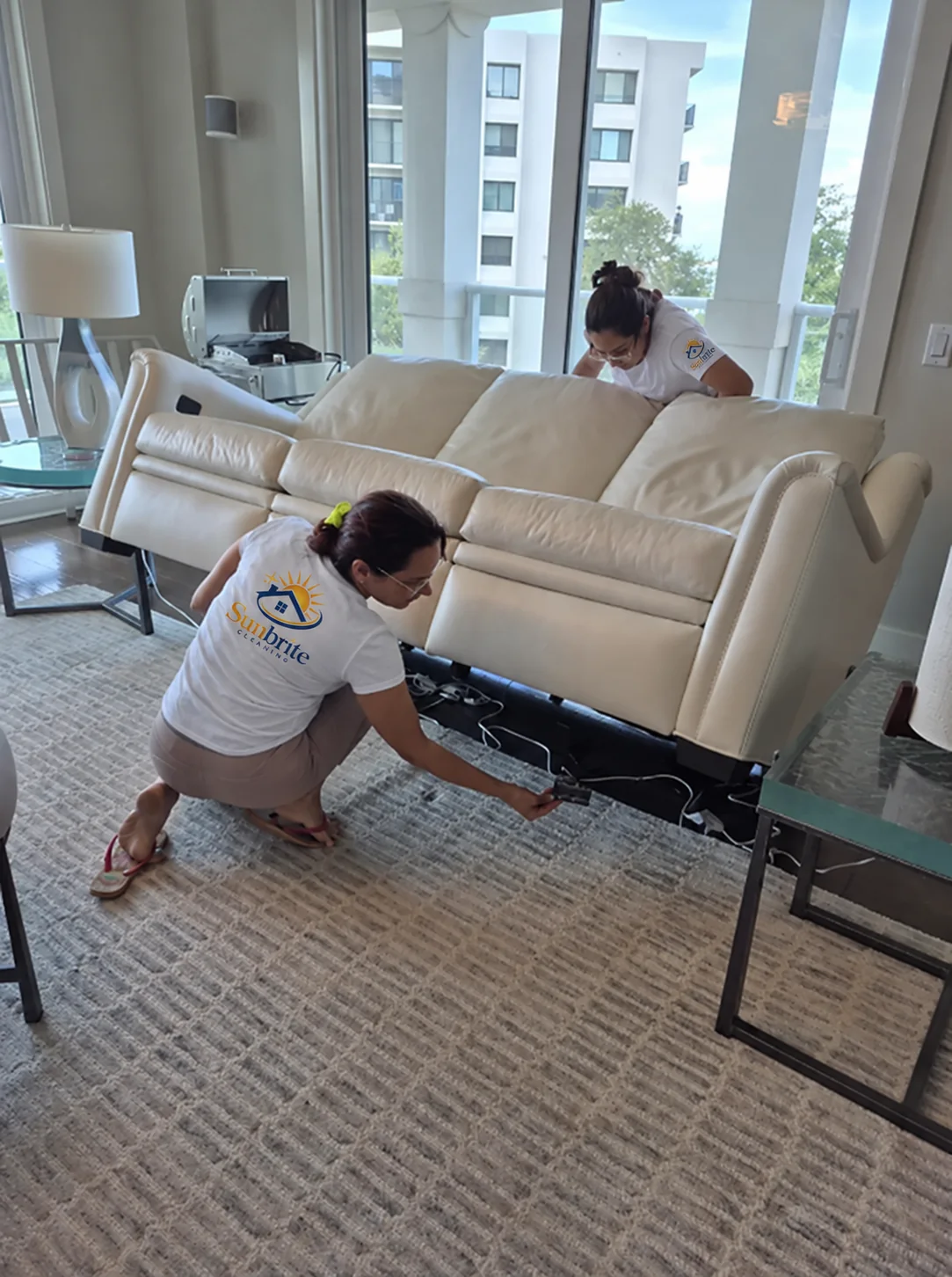 Two Sunbrite Cleaning LLC team members lifting a leather sofa to clean underneath it