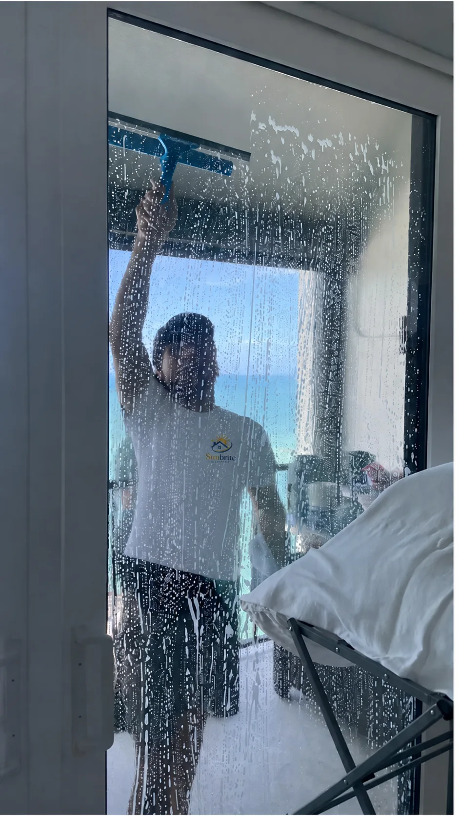 Sunbrite Cleaning LLC team member squeegeeing a soapy glass sliding door with an ocean view